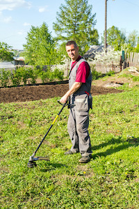Mann mit Akku Rasentrimmer mäht den Rasen